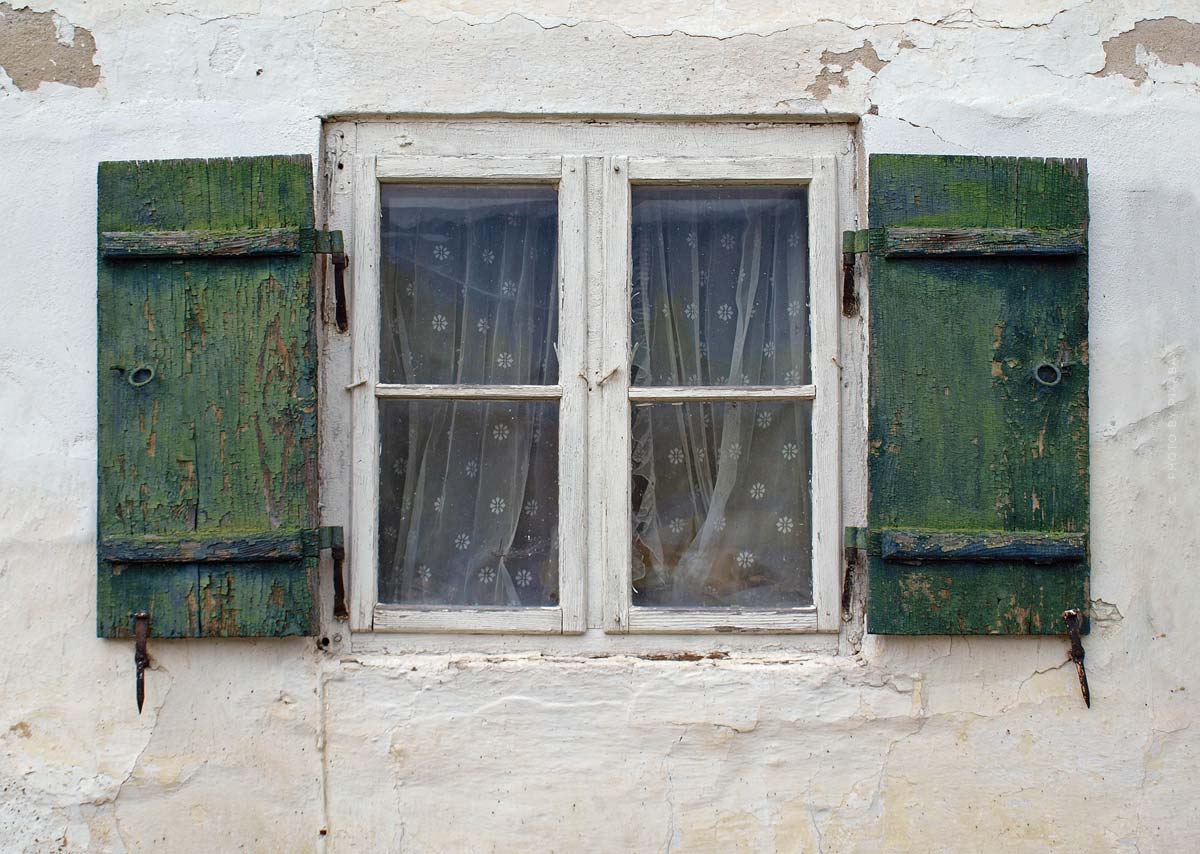 Hier sehen Sie veraltete Fenster mit grünen Holzfensterläden, sowie eine bröckelnde Fassade, die erneuert werden muss. 
